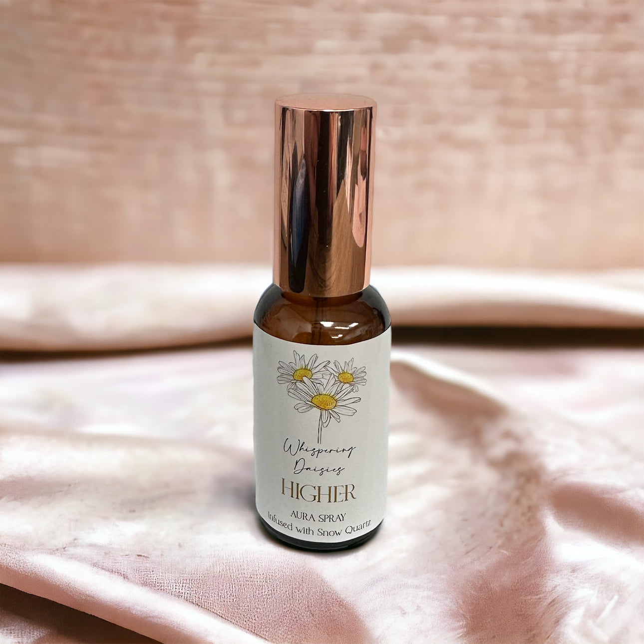 A 30ml glass bottle of 'Higher - White Quartz Crystal - Aura Spray' with a copper-colored cap, labeled with a white and yellow design, placed on a pink fabric surface.
